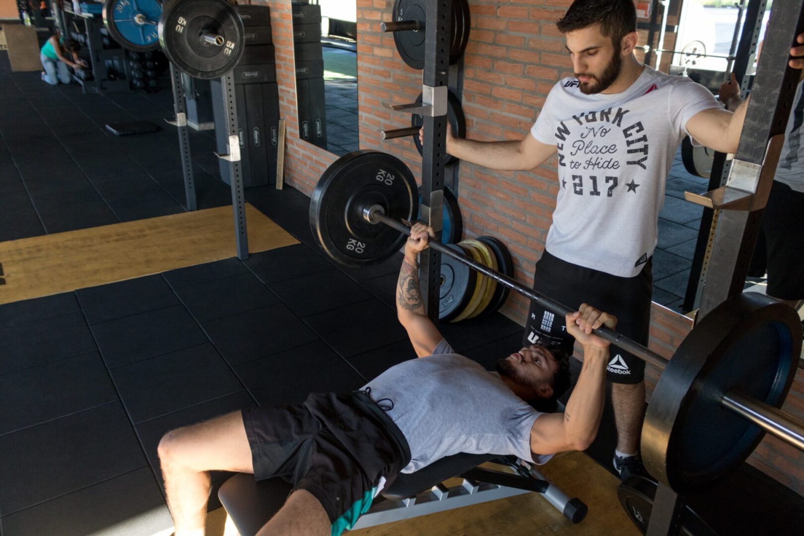 A man is lifting a barbell in front of another man.